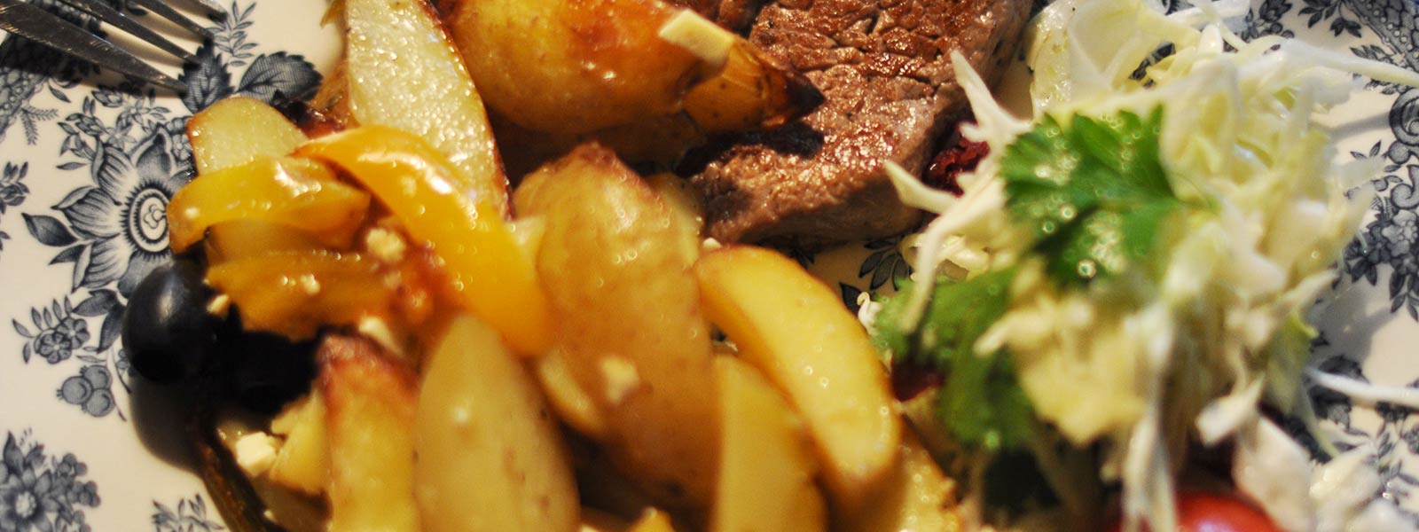 Obiad na talerzu: pieczony schab, ziemniaki, kolorowe papryki i świeża sałata.